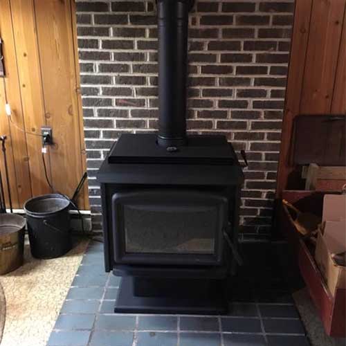 Black, Freestanding Wood Stove atop black tile with black brick heat wall behind