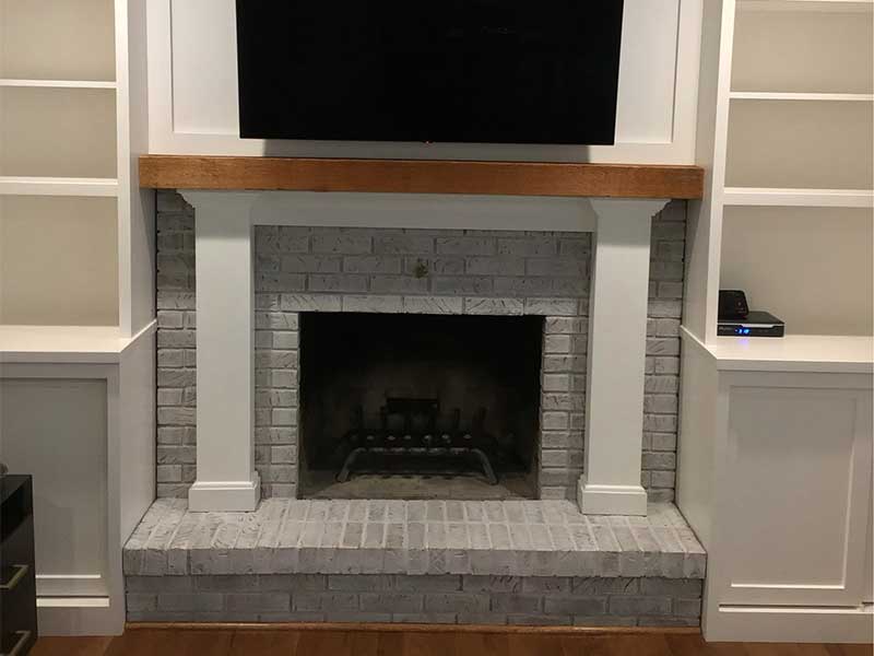Fireplace with white washed brick surround hearth and white and pine wood mantel after facelift