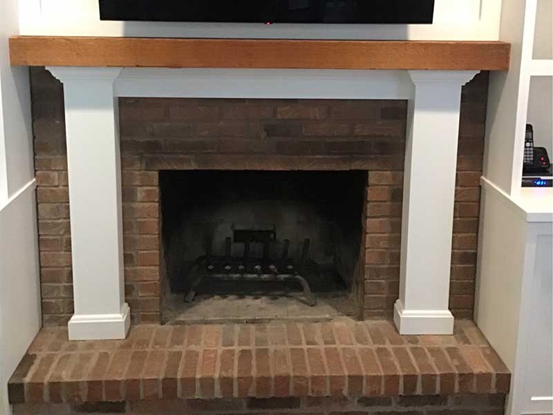 Fireplace with red brick surround hearth and white and pine wood mantel before facelift