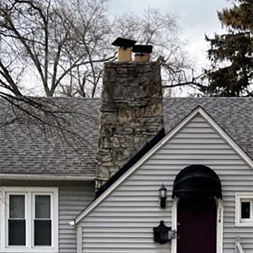 Dirty, stained stoned chimney with double flue and deteriorating chimney caps