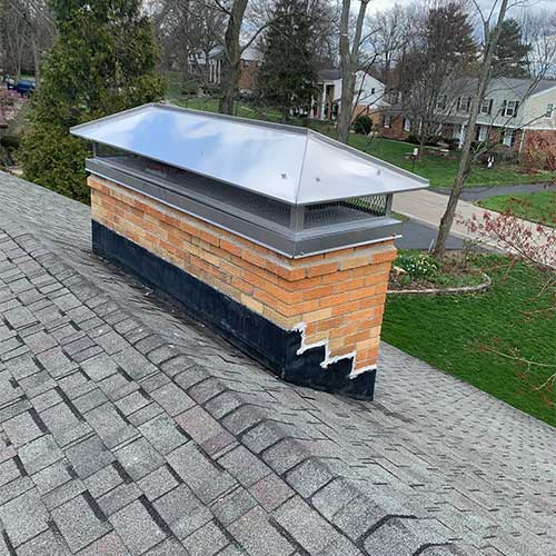 Custom-fitted stainless steel chimney cap on brick chimney