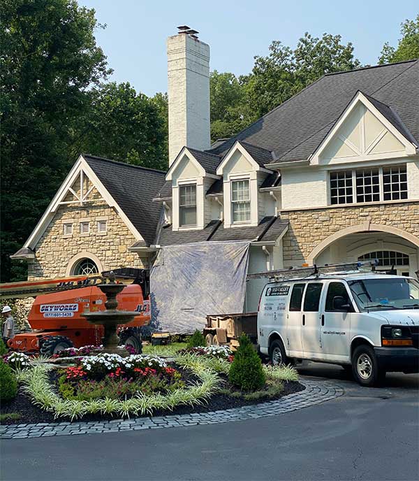 Mid-Valley Chimney - Contact Us - Nice stone facing on the home with a truck in the foreground and tarp over the front porch - a boom to the left and several peaks and tall chimney on the home