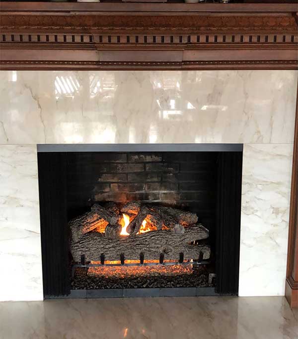 Fireplace with updated logs, black bricks and fire rocks white marble surround and chestnut wood mantel after facelift