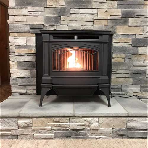 Black gas stove sitting atop stone hearth with stone heat wall behind it