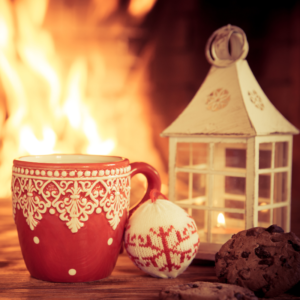 a christmas mug, ornament, and lantern in front of a lit fireplace