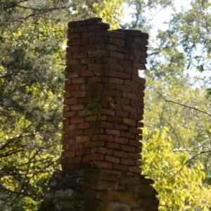 a crumbling and leaning brick masonry chimney with missing bricks