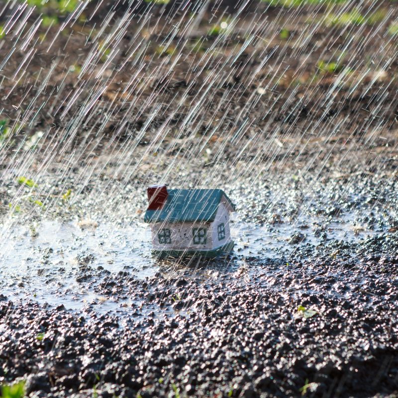 a small toy house sitting in the mud with rain falling on it