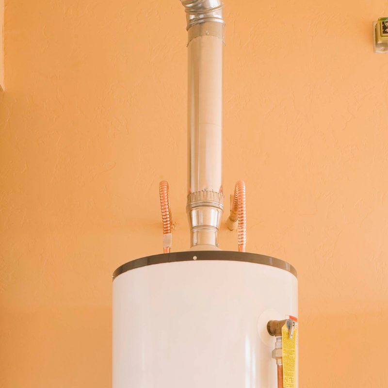 a flue coming out of the top of a water heater in front of a light orange wall
